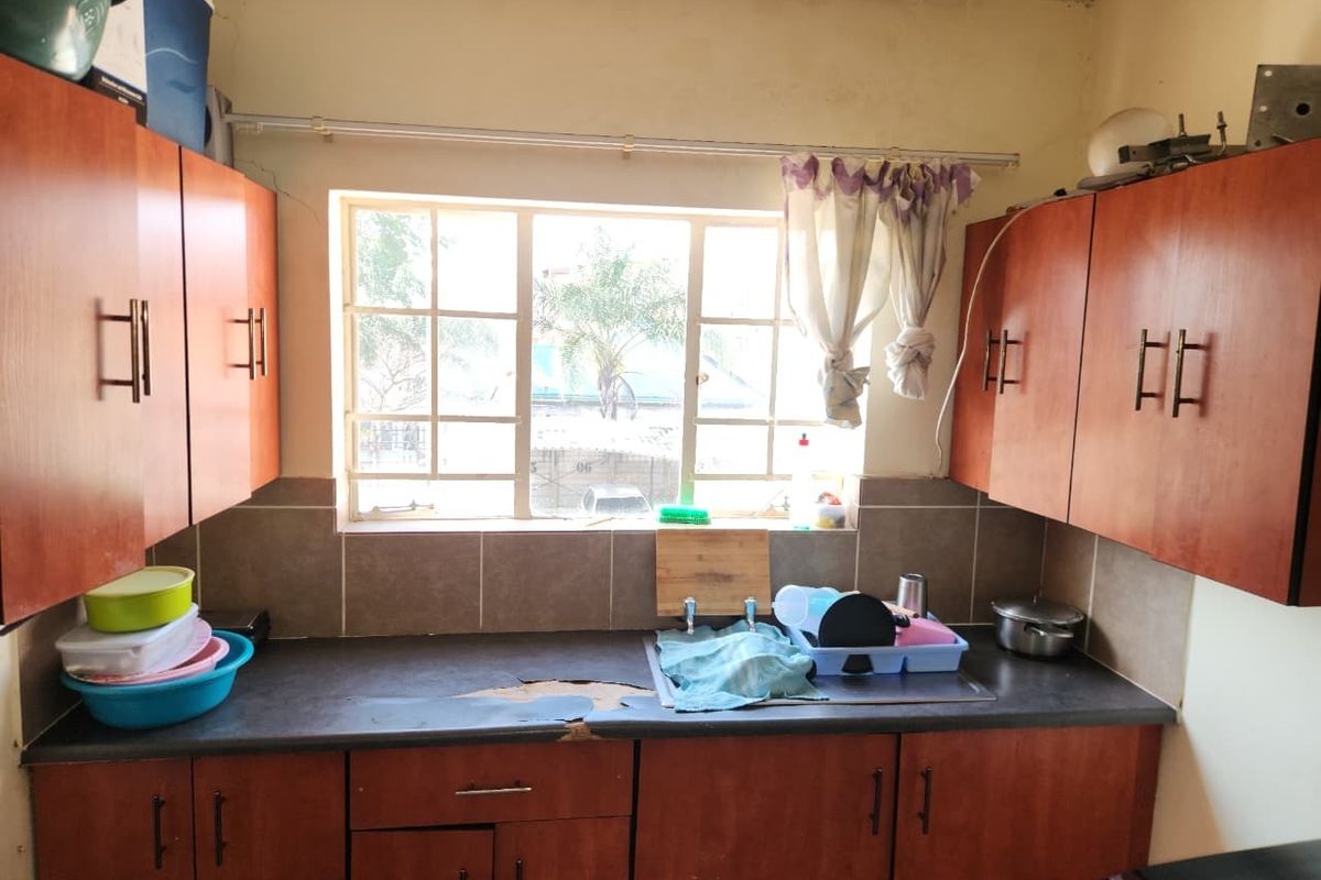 A compact kitchen featuring wood-look cabinetry, a tiled backsplash, and a stainless steel sink, currently showing signs of wear on the countertop surface.