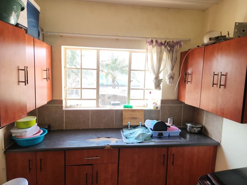 A compact kitchen featuring wood-look cabinetry, a tiled backsplash, and a stainless steel sink, currently showing signs of wear on the countertop surface.