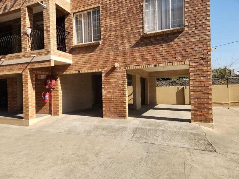 Ground level covered parking area featuring face brick construction and concrete flooring, located beneath an apartment balcony.