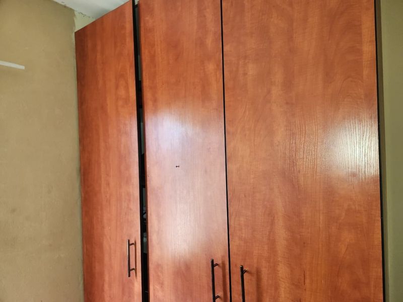A bedroom featuring a built-in wooden wardrobe with unfinished wall surfaces requiring attention.