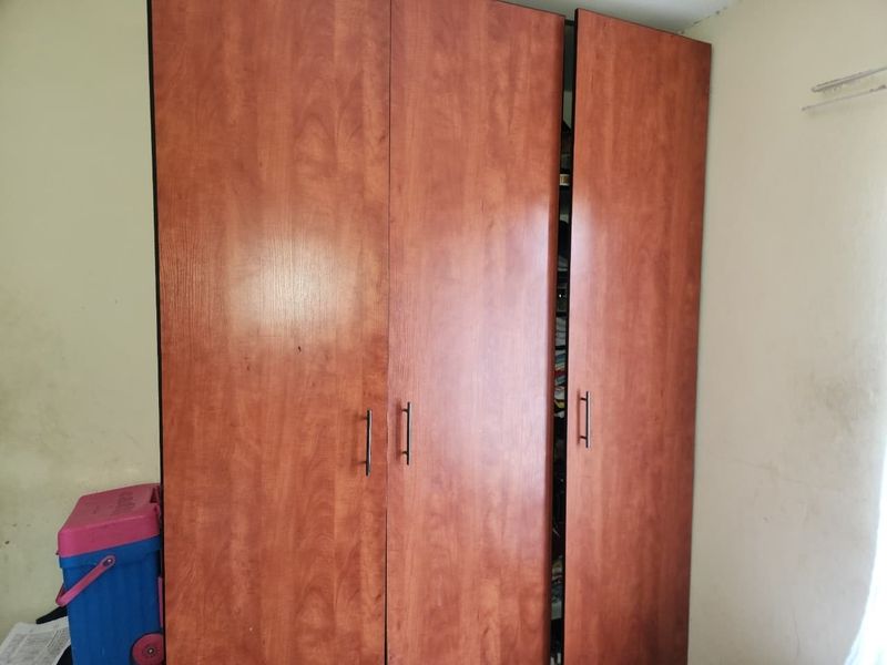 A bedroom featuring a large built-in wooden wardrobe with visible wear and wall staining requiring maintenance.