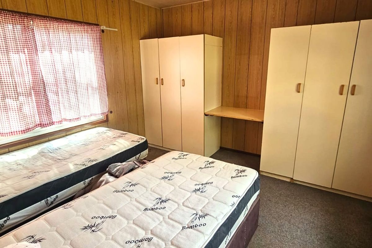 A bedroom featuring wood-paneled walls, built-in wardrobes with an integrated desk, and carpeted flooring.