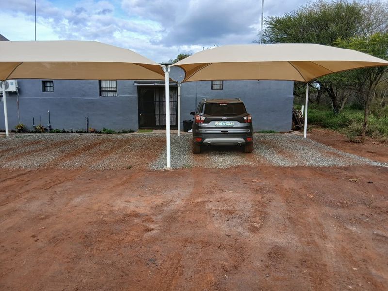 Exterior view of the property featuring a double shade sail carport structure over a gravel driveway and a grey painted facade.