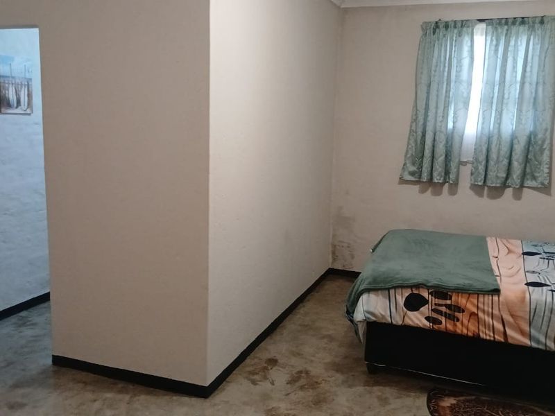A bedroom featuring concrete flooring and an installed air conditioning unit, showing signs of wall staining and dampness requiring maintenance.