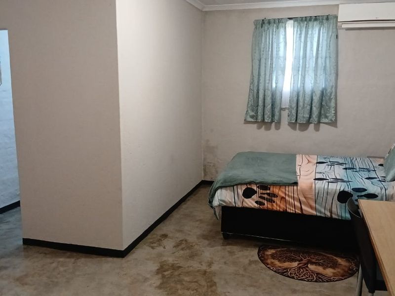 A bedroom featuring concrete flooring and an installed air conditioning unit, showing signs of damp on the lower wall section.