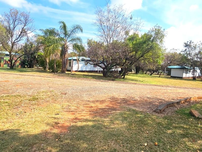A spacious outdoor area featuring a gravel driveway, established trees, and a large garden surrounding the property structures.
