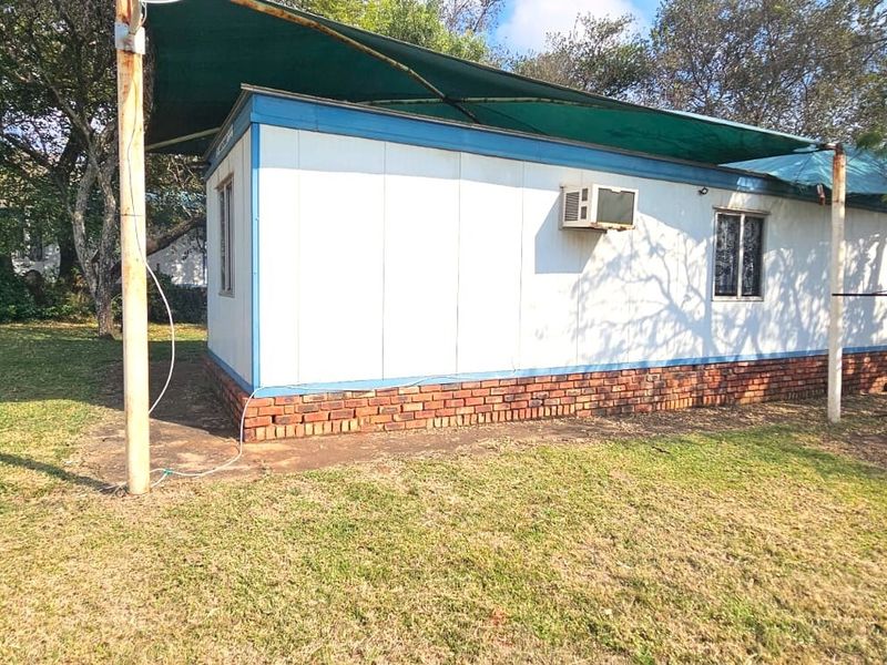 Rear view of a prefabricated structure featuring a brick foundation, metal siding, and a shade cloth awning covering the exterior area.