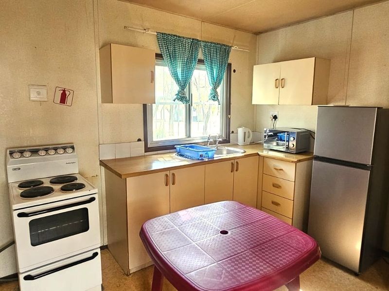 A compact, functional kitchen featuring original cabinetry, laminate countertops, a stainless steel sink, and a freestanding stove, offering potential for modern renovation.
