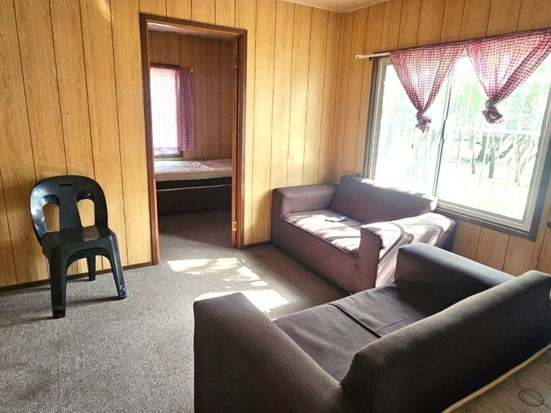 A living room featuring dated wood paneling, carpet flooring, and a sliding window, providing a functional space with potential for modernization.