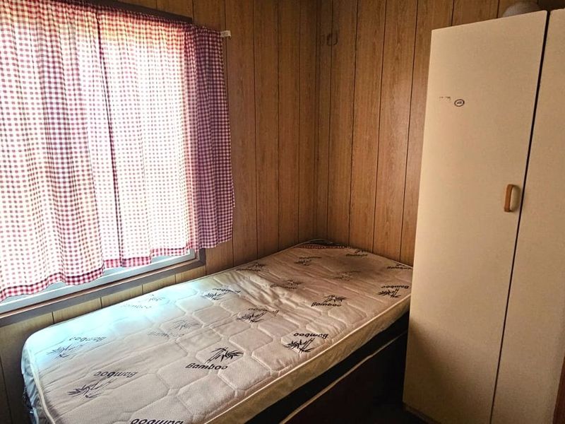 A bedroom featuring wood-paneled walls and a built-in wardrobe, offering a dated aesthetic that could benefit from modern updates.