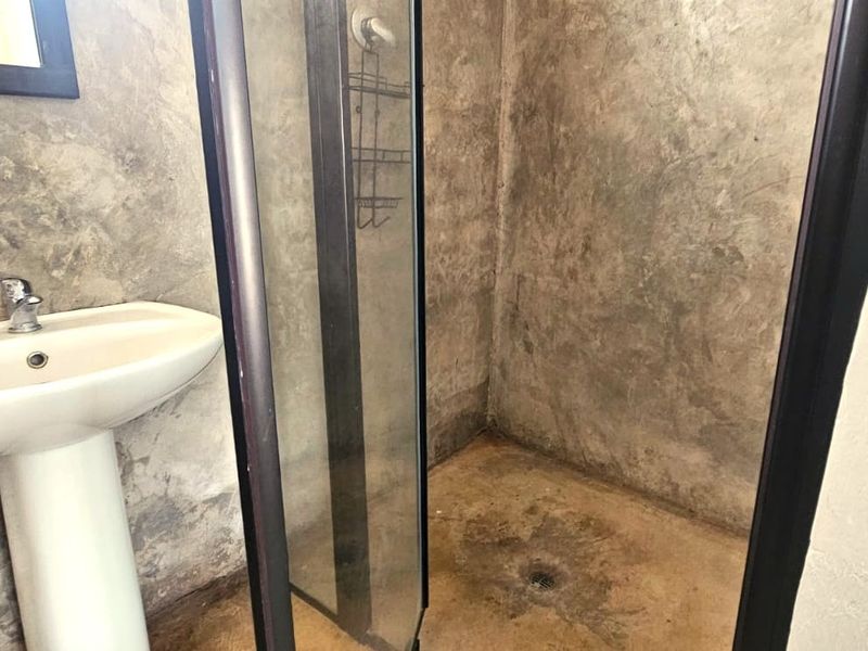 A bathroom featuring a pedestal basin and a shower enclosure with industrial-style cementitious wall finishes.