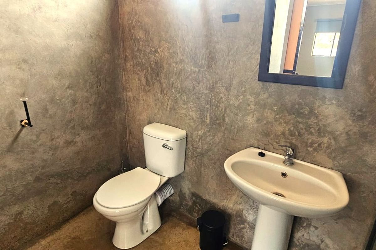 A compact bathroom featuring a pedestal basin, toilet, and raw concrete-style wall finishes, currently awaiting final touches and fixture completion.