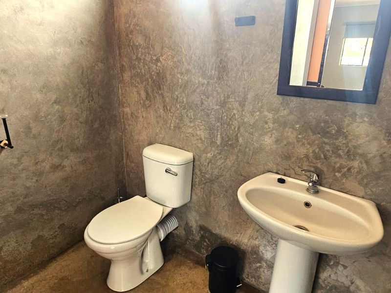 A compact bathroom featuring a pedestal basin, toilet, and raw concrete-style wall finishes, currently awaiting final touches and fixture completion.