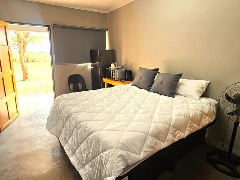 A compact bedroom featuring concrete flooring, a timber entrance door, and a roller blind, providing direct access to the exterior.