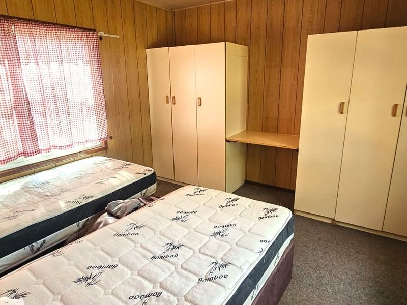 A bedroom featuring wood-paneled walls, built-in wardrobes with an integrated desk, and carpeted flooring.