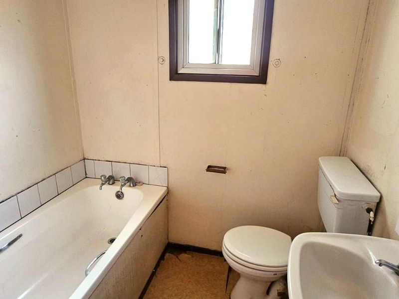 A dated bathroom featuring a standard bathtub, toilet, and pedestal sink, requiring cosmetic updates and modernization of finishes.