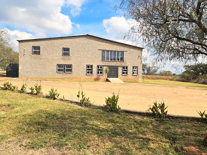 A wide-angle view of a two-story brick building featuring multiple windows and a concrete entrance ramp, set within a large open landscape.