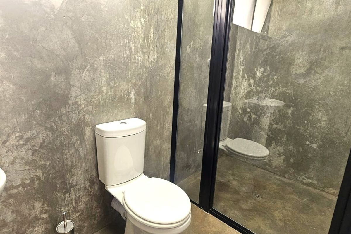 Modern bathroom featuring industrial-style concrete walls, a wall-mounted basin, and a walk-in shower with a sleek black frame.