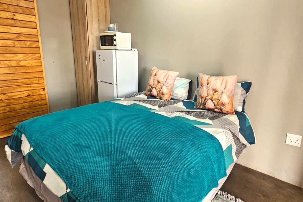 A compact bedroom featuring concrete flooring, a built-in cupboard, and a wooden door leading to an adjacent space.