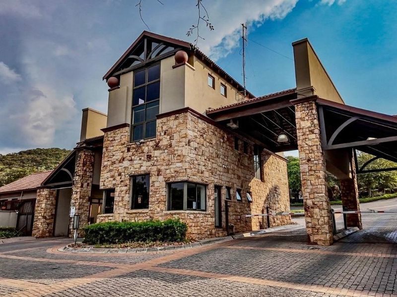 A well-maintained stone-clad security entrance gatehouse featuring a paved driveway and covered access point for a residential estate.