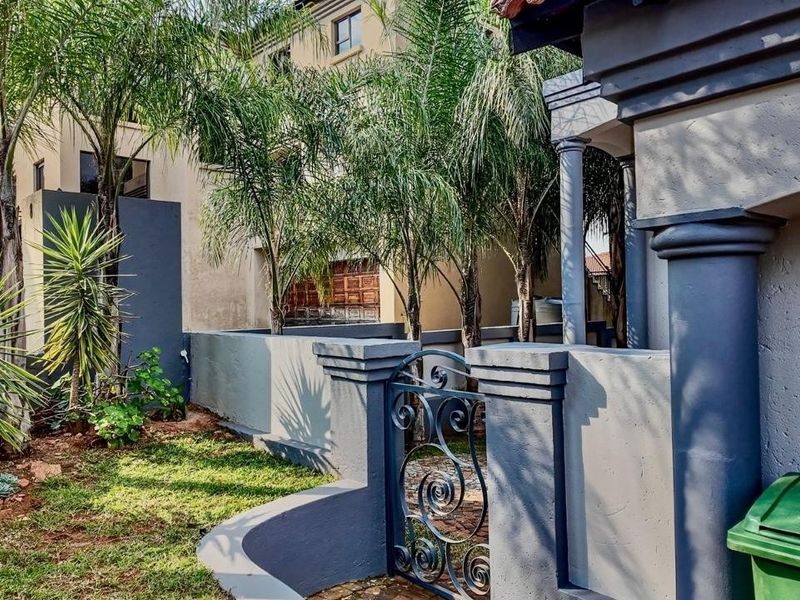 Front entrance area featuring a decorative wrought iron gate, masonry boundary walls, and established landscaping leading to the main dwelling.