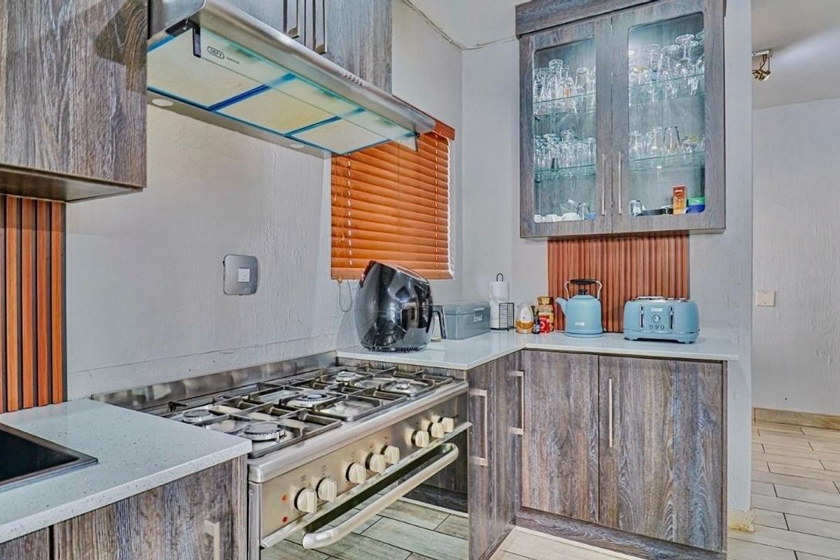 A functional kitchen featuring wood-grain cabinetry, stone countertops, a gas stove with an extractor fan, and glass-fronted display cabinets.