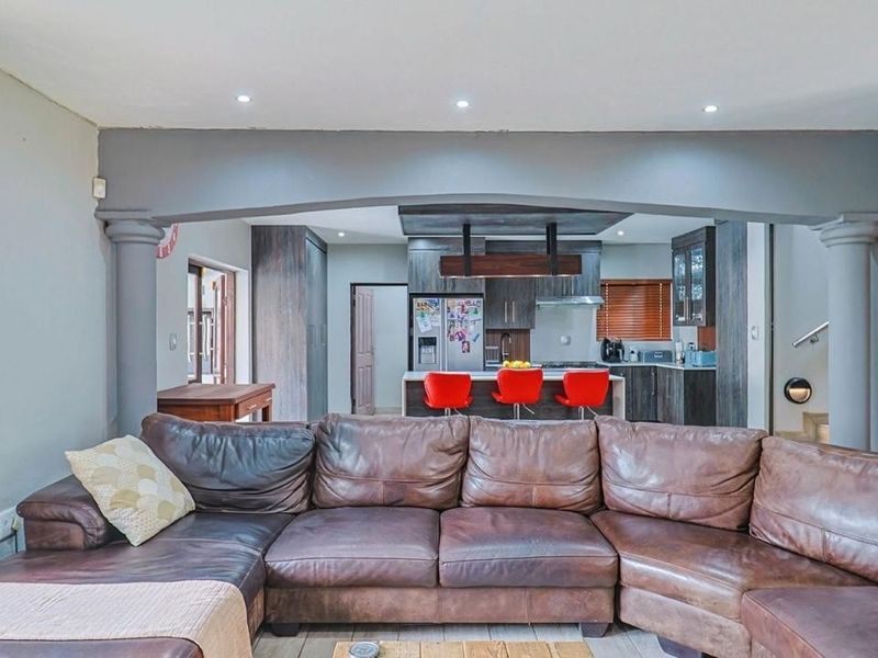 Open-plan living area featuring a modern kitchen with a central island, dark cabinetry, and recessed lighting, seamlessly connected to the lounge space.