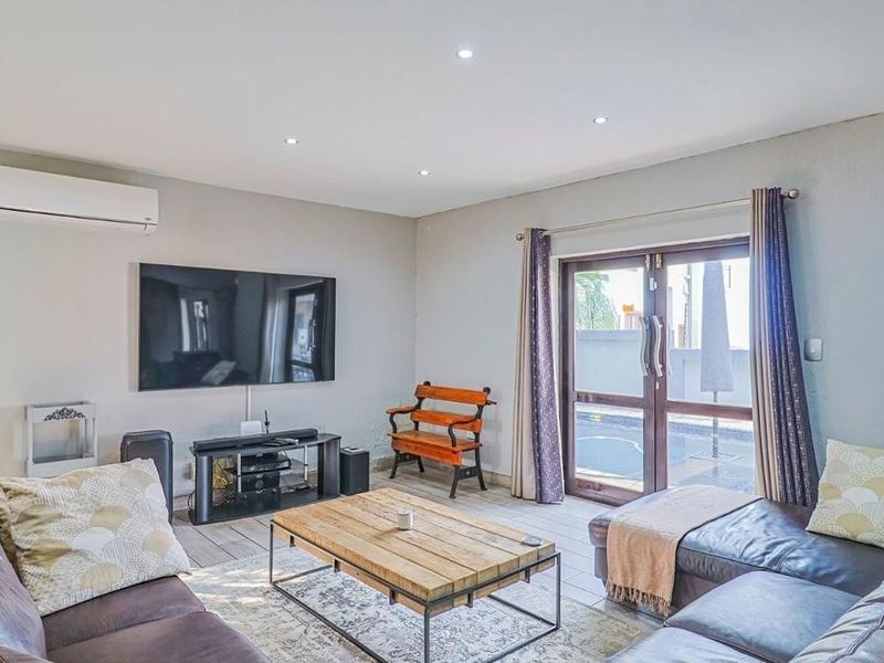 A well-lit living room featuring tiled flooring, recessed downlighting, a wall-mounted air conditioning unit, and direct access to the outdoor pool area.