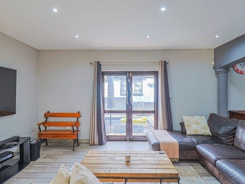 Spacious living room featuring tiled flooring, recessed downlights, and double glass doors providing direct access to the outdoor pool area.