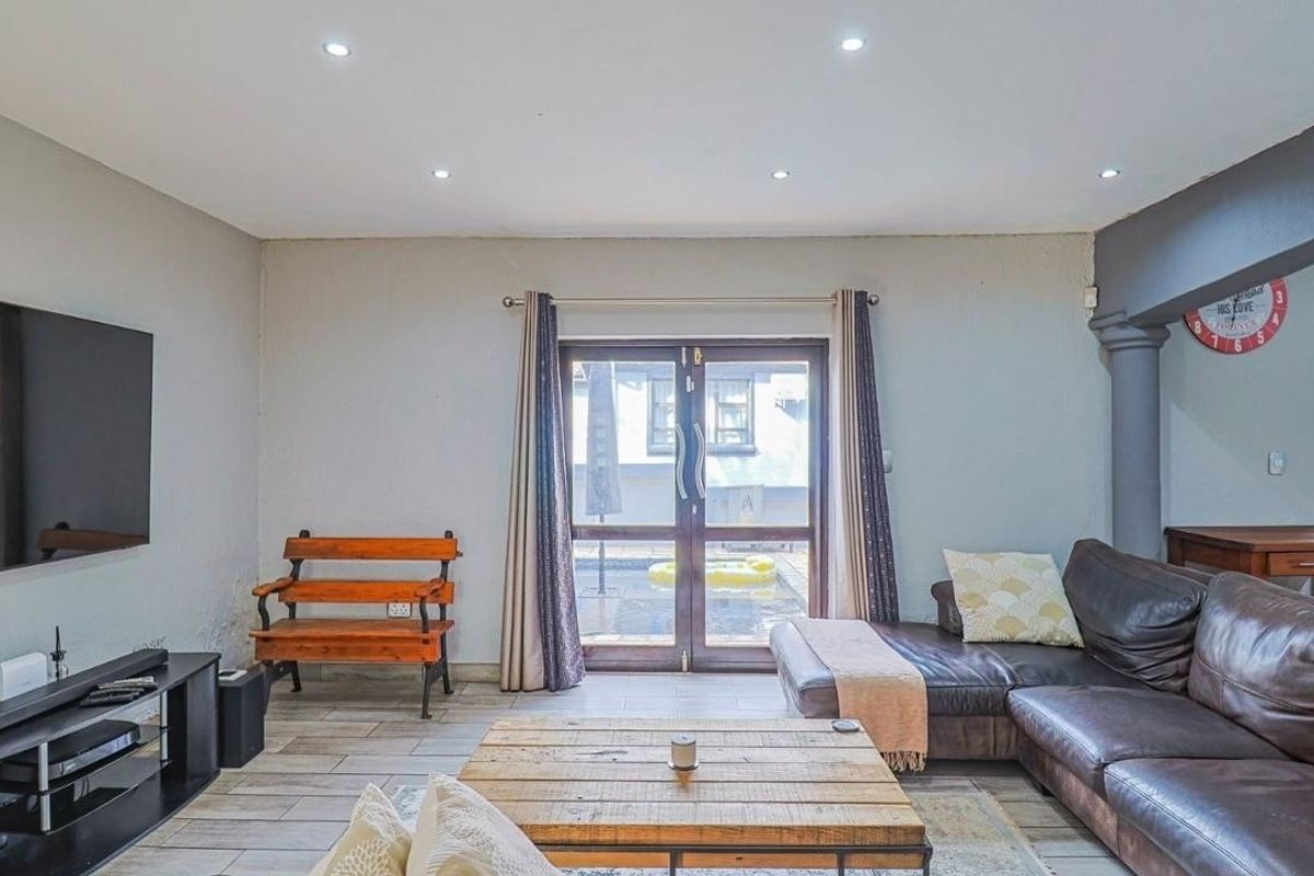 Spacious living room featuring tiled flooring, recessed downlights, and double glass doors providing direct access to the outdoor pool area.