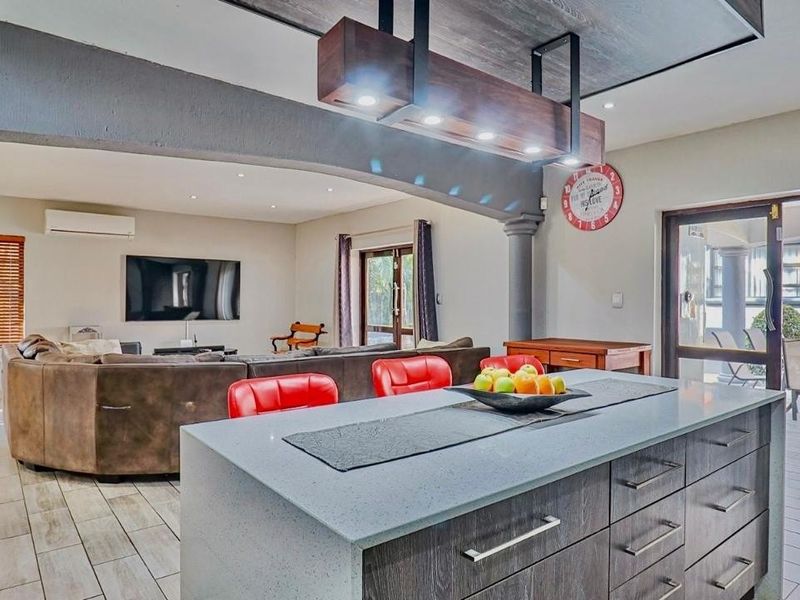 Spacious open-plan living area featuring a modern kitchen island with stone countertops, tiled flooring, and seamless flow to the outdoor patio through sliding doors.