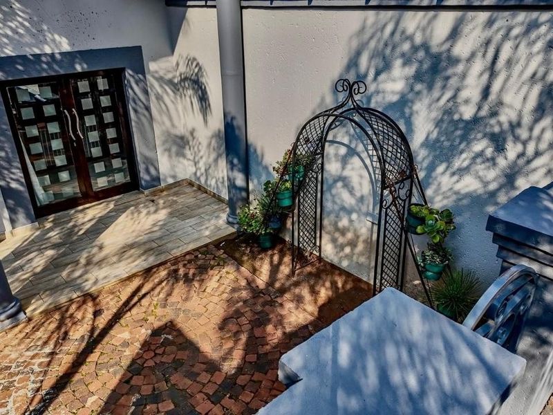 A paved outdoor patio area featuring a double glass entrance door, structural columns, and a decorative metal garden archway.