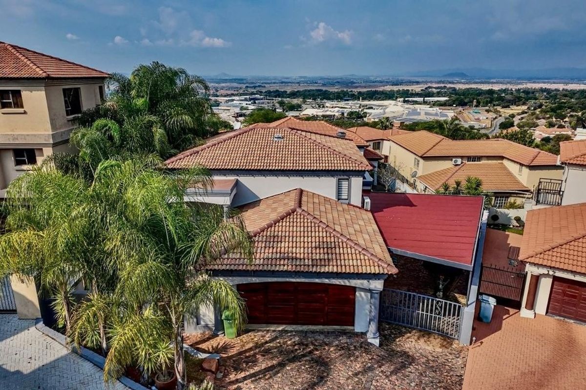 Aerial view of the property showcasing the terracotta tiled roof, paved driveway, double garage, and covered carport area within a residential estate.