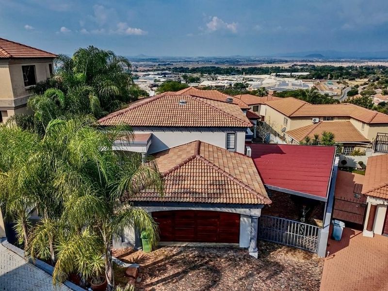 Aerial view of the property showcasing the terracotta tiled roof, paved driveway, double garage, and covered carport area within a residential estate.