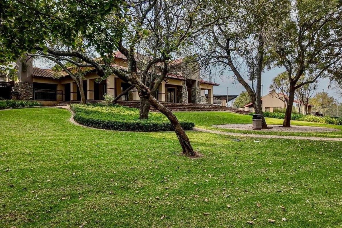 Spacious rear garden featuring mature trees, manicured lawns, and a covered patio area with stone architectural detailing.
