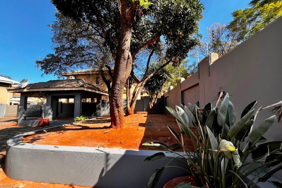 A private rear garden area featuring a mature tree, a raised retaining wall, and a covered patio space with perimeter walling and electric fencing.