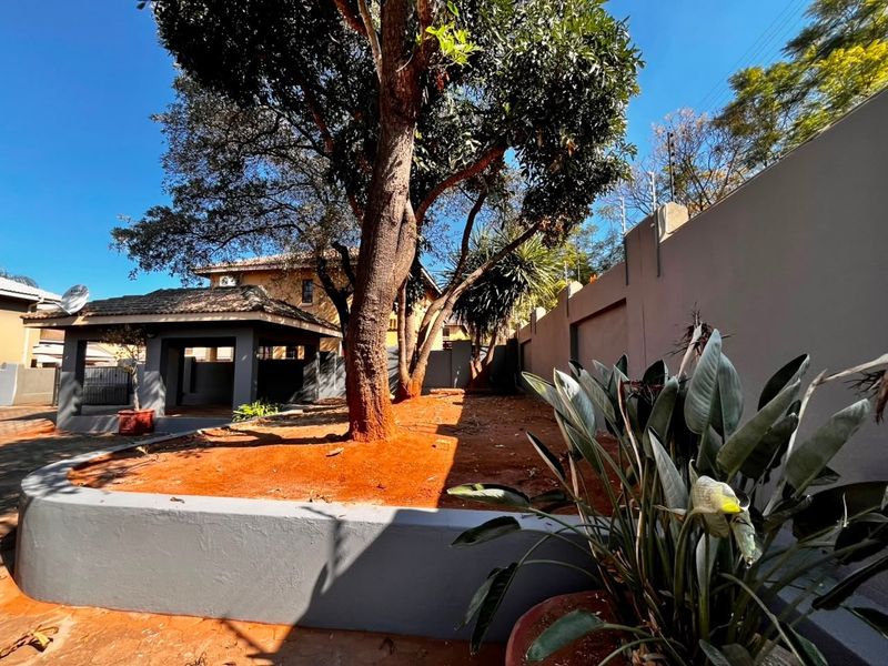 A private rear garden area featuring a mature tree, a raised retaining wall, and a covered patio space with perimeter walling and electric fencing.