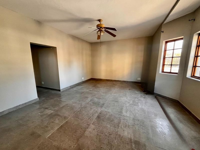 An empty, spacious living area featuring neutral tiled flooring, a ceiling fan, and timber-framed windows providing natural light.