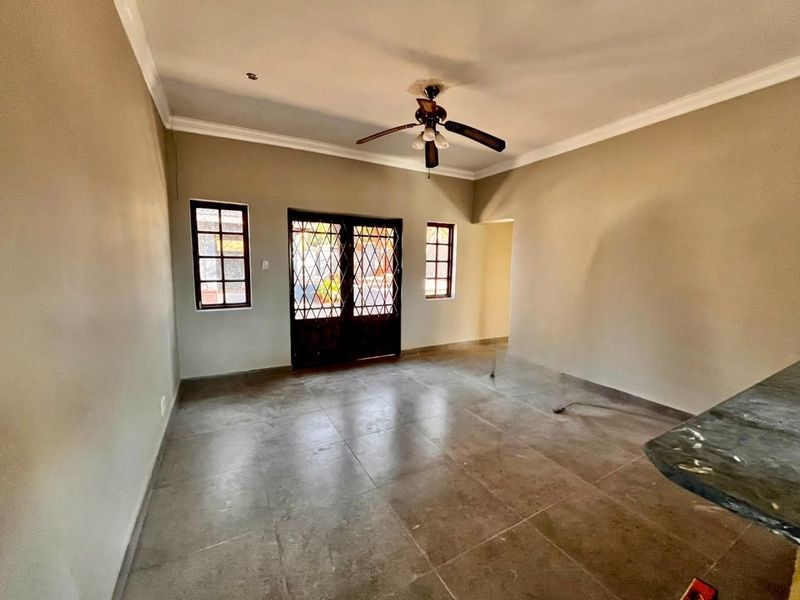 An empty living area featuring tiled flooring, a ceiling fan, and a security gate leading to the exterior.