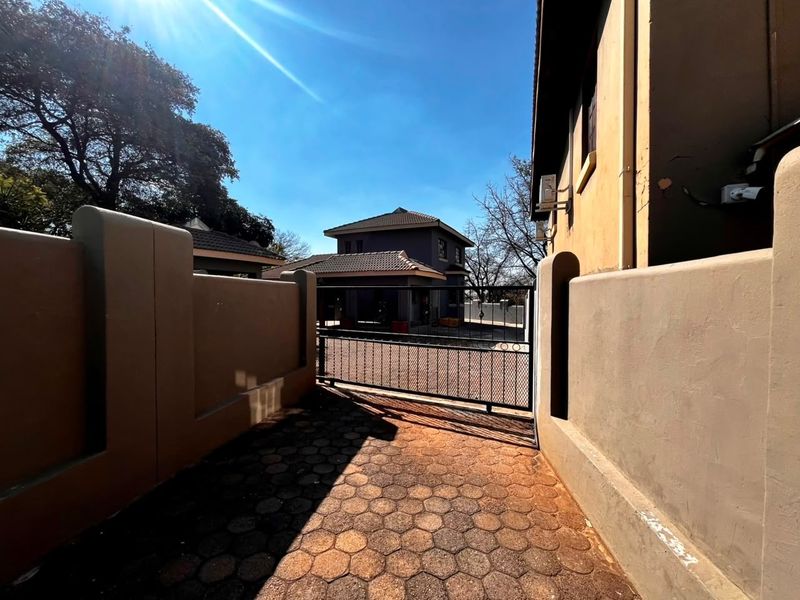 Front entrance area of the townhouse featuring a paved driveway, boundary walls, and a metal security gate.