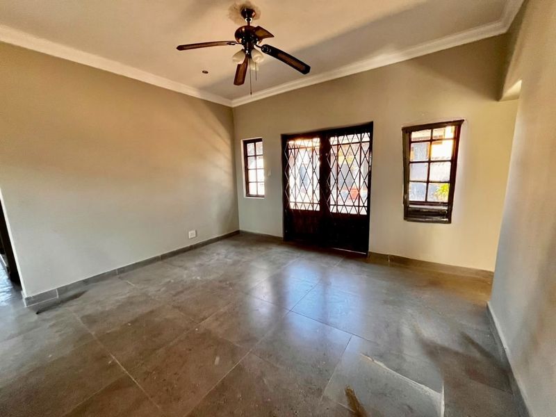 An empty living room featuring tiled flooring, a ceiling fan, and security gates leading to the exterior.