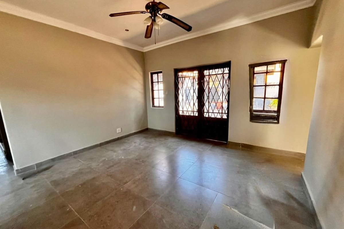 An empty living room featuring tiled flooring, a ceiling fan, and security gates leading to the exterior.