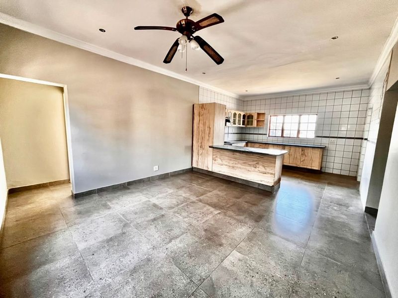Spacious open-plan living and kitchen area featuring neutral tiled flooring, built-in wooden cabinetry, and a central kitchen island with a breakfast counter.