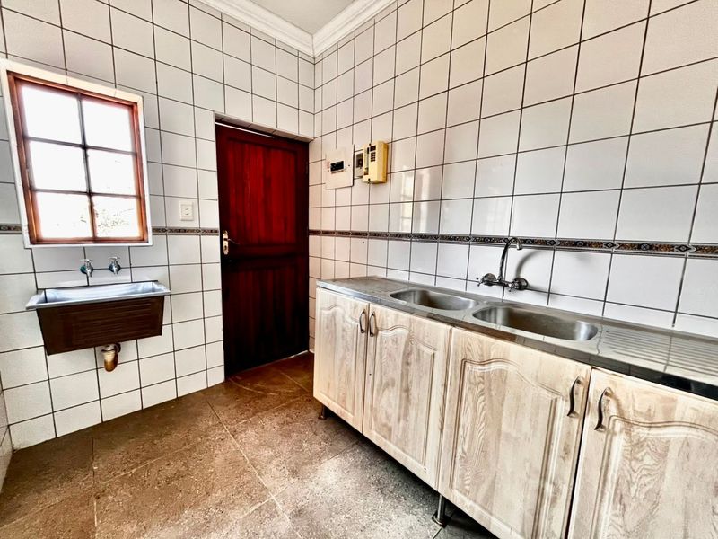 A functional scullery area featuring tiled walls, double stainless steel sink, additional utility sink, and wooden cabinetry with direct access to an exterior door.