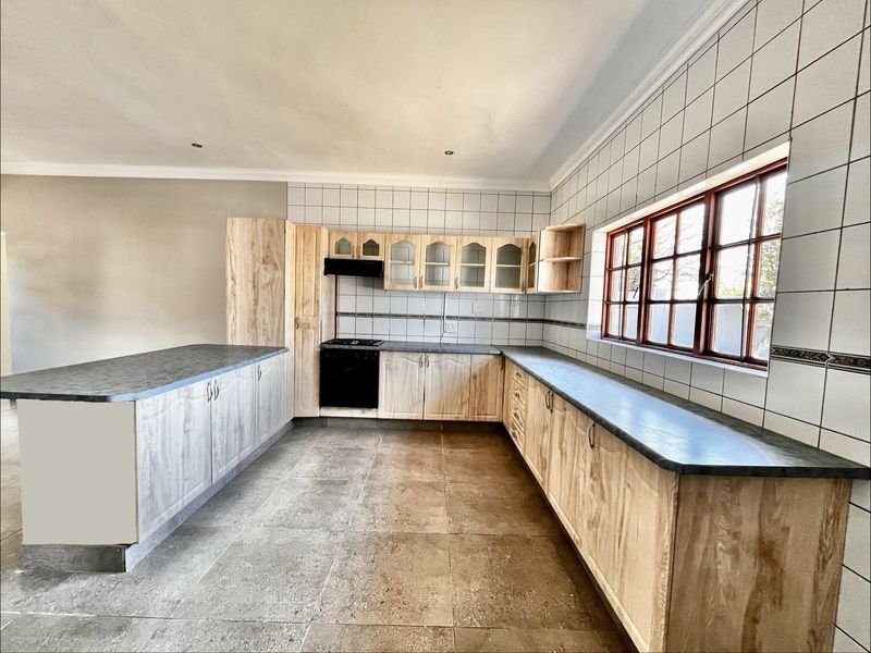 Spacious kitchen featuring light wood-look cabinetry, dark laminate countertops, tiled backsplash, and built-in oven, offering a functional layout ready for modern updates.