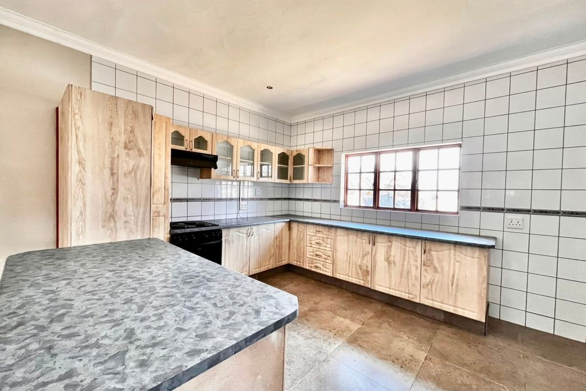 A spacious, empty kitchen featuring light wood-look cabinetry, laminate countertops, tiled backsplash, and tiled flooring, offering a functional layout ready for modernization.