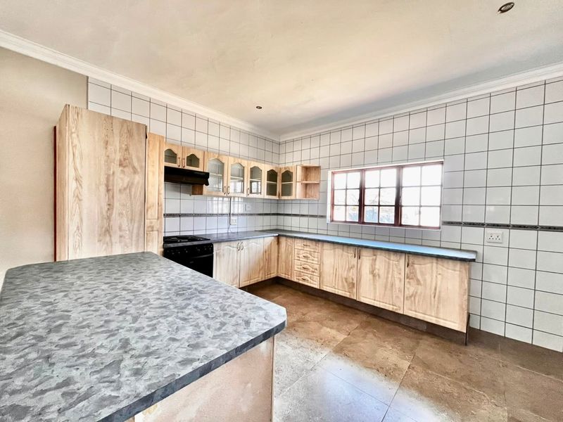 A spacious, empty kitchen featuring light wood-look cabinetry, laminate countertops, tiled backsplash, and tiled flooring, offering a functional layout ready for modernization.