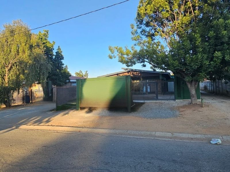 Street view of the property entrance featuring a metal security gate, perimeter fencing, and a gravel driveway access point.