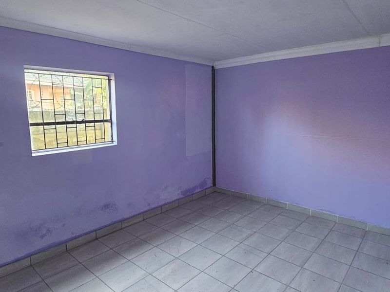 An empty bedroom featuring tiled flooring, security bars on the window, and purple painted walls showing signs of moisture damage.