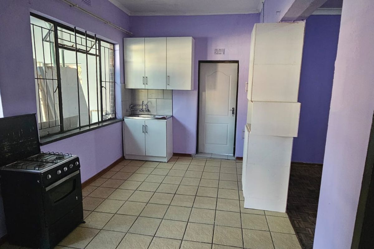 A basic kitchen area featuring tiled flooring, built-in cabinetry, a stainless steel sink, and security bars on the windows.